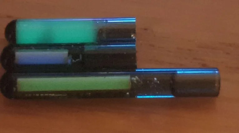 Cyberpunk-style glass implants, featuring one with glow-in-the-dark strontium aluminate powder and two with tritium rods, showcasing advanced biohacking and implant design.