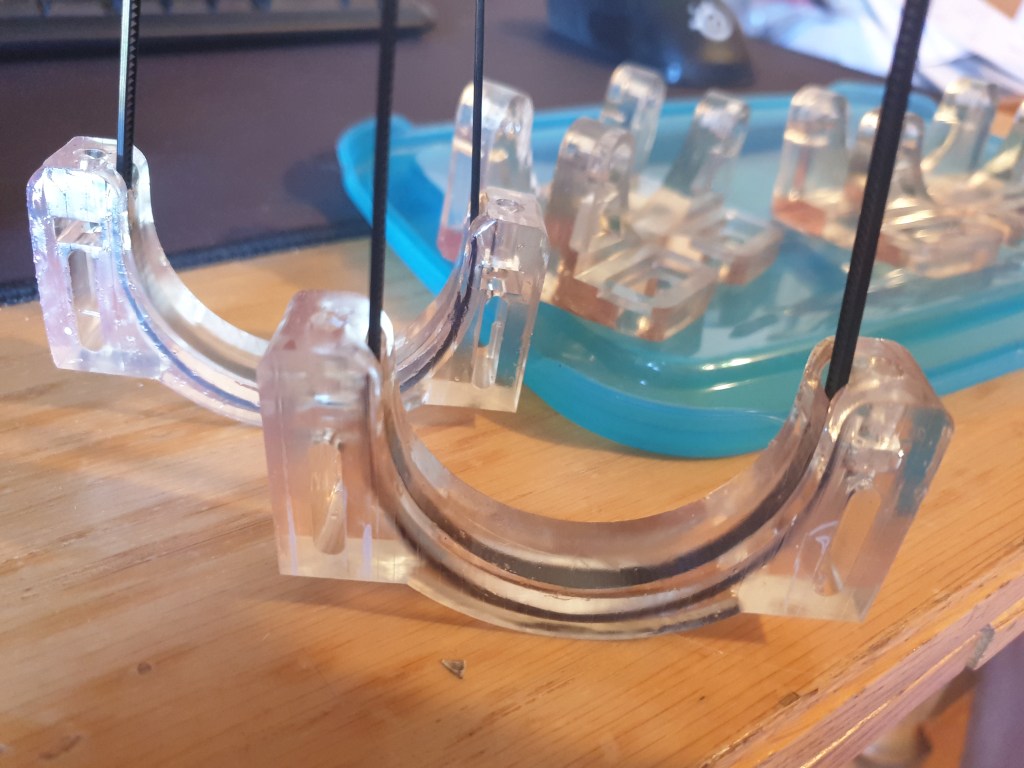 3D-printed resin holders with zip ties attached, securing components for CO2 laser setup in DIY biohacking and implant sealing projects.