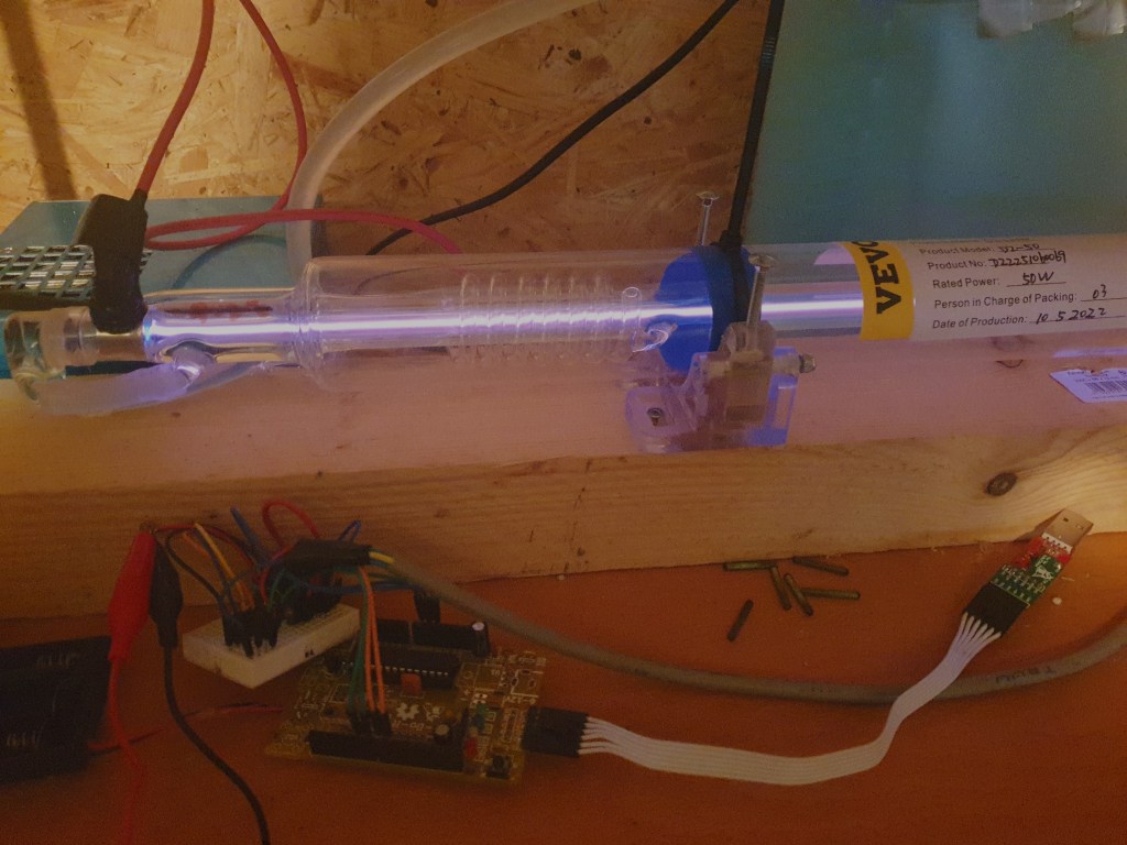High Power CO2 laser turned on, emitting a fantastic glow, with the Arduino control unit in the background, highlighting the DIY biohacking setup.